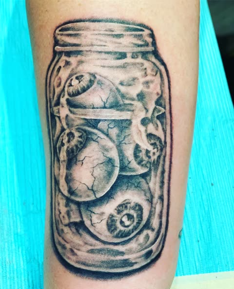 Jar of eyeballs tattoo in black ink with stipple shading on a forearm