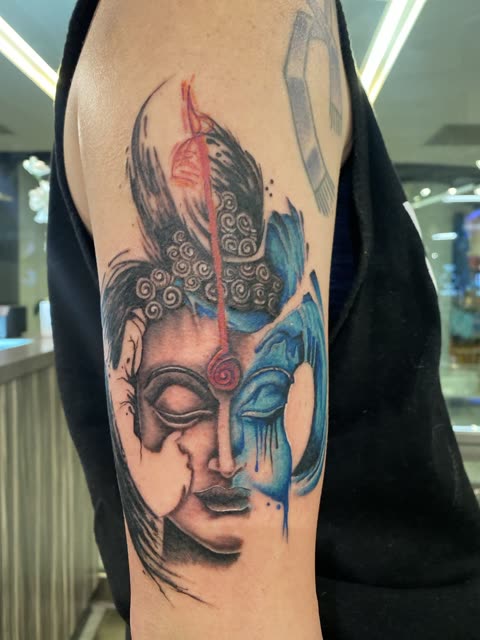Split face tattoo, half in black shading and half in blue with a red line down the center, on an upper arm