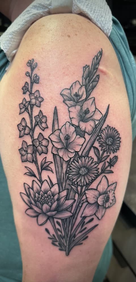 Birth flower bouquet tattoo with gladiolus, water lily and daffodil, black whip shading, on an upper arm