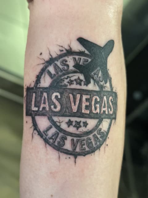 Las Vegas travel stamp tattoo with an airplane, black ink, on a forearm