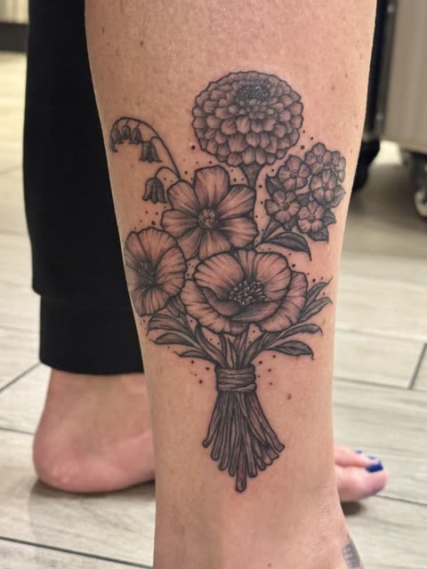 Wildflower bouquet tattoo with wrapped stems, black stipple shading, on a calf