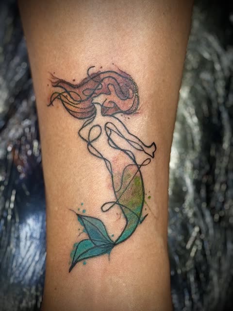 Continuous line mermaid tattoo with red and green watercolor washes on a lower leg