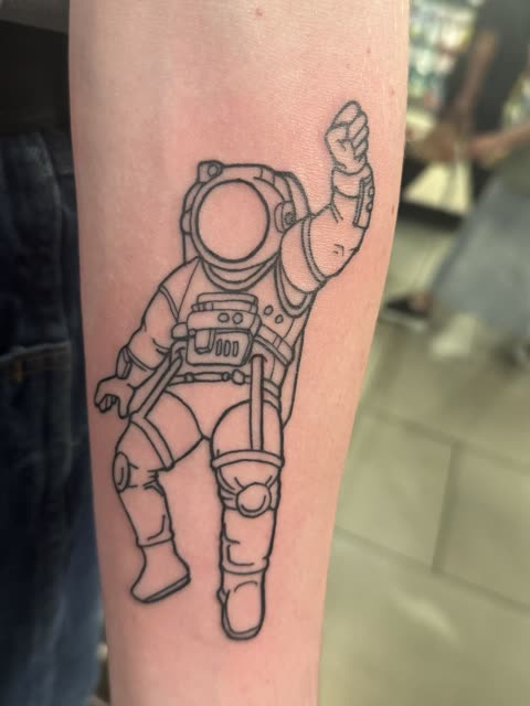 Astronaut tattoo raising a fist, clean linework, on a forearm