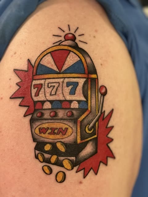 Traditional slot machine tattoo hitting triple sevens with gold coins, full color, on a shoulder
