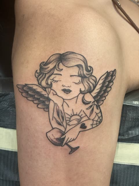 Traditional cherub tattoo with tattooed arms and a wine glass, black shading, on a thigh