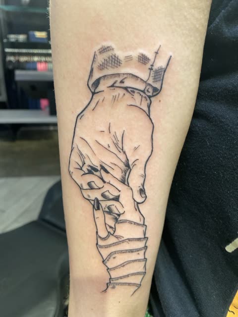 Tattoo of an adult hand holding a child's hand, clean linework, on a forearm