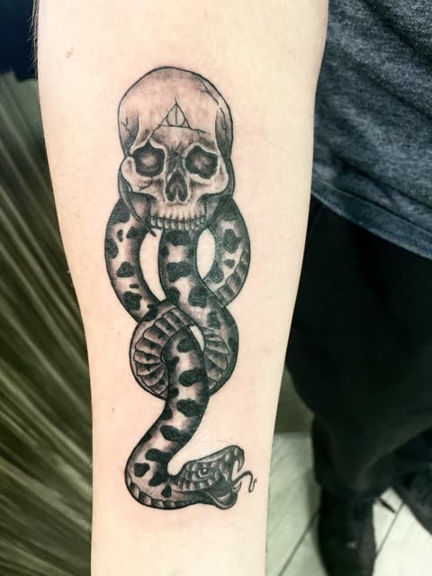 Skull and snake tattoo with the snake winding through the jaw, black shading, on a forearm