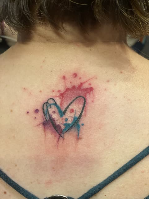 Sketch style heart tattoo with red and blue watercolor splashes on the upper back