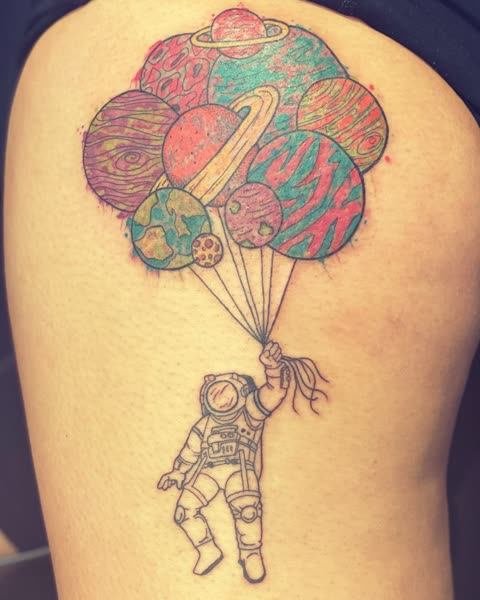 Astronaut tattoo floating from a bunch of planet balloons, color over linework, on a thigh