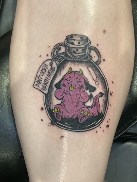 Cartoon monster in a corked bottle tattoo with a warning tag, full color, on a lower leg