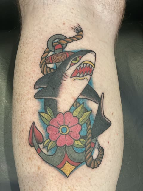 Traditional shark and anchor tattoo with rope and a pink flower, full color, on a calf