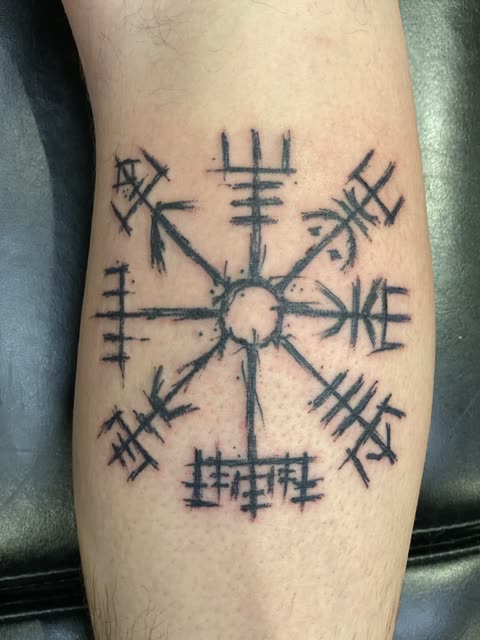 Norse compass tattoo in brushed black strokes on a calf