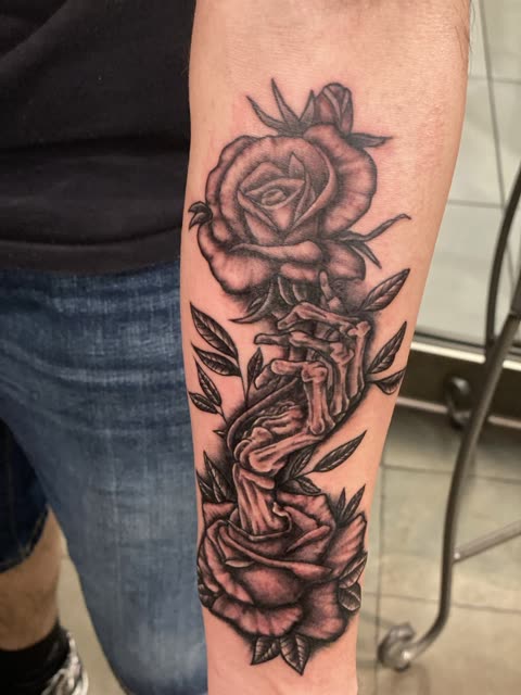 Skeleton hand and roses tattoo in black shading down a forearm