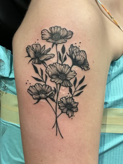 Cosmos flowers tattoo in black whip shading on an upper arm