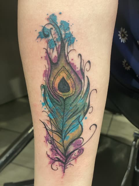 Peacock feather tattoo in blue, green and purple watercolor on a forearm