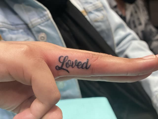 The word Loved tattooed in script along the side of a finger