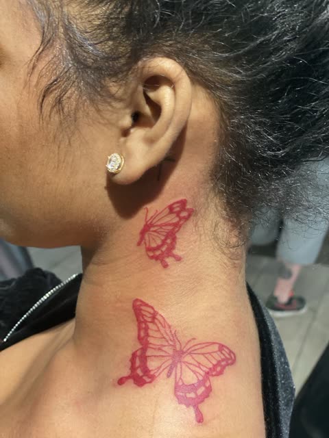 Two red ink butterfly tattoos on the side of the neck