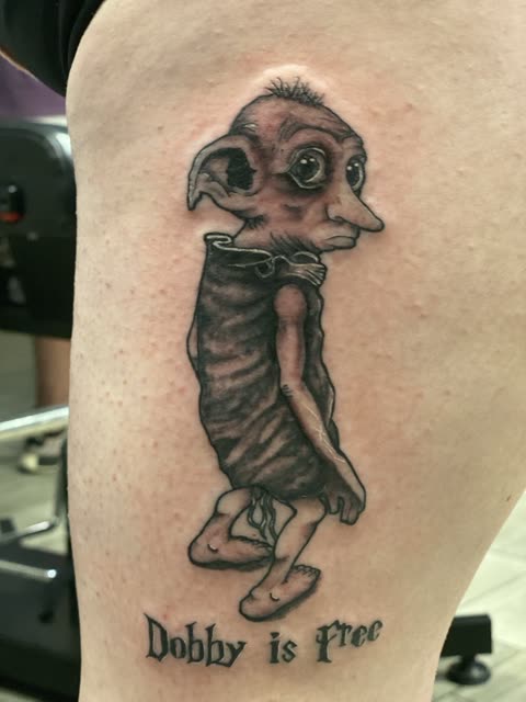 House elf tattoo with Dobby is Free in script, black shading, on a thigh