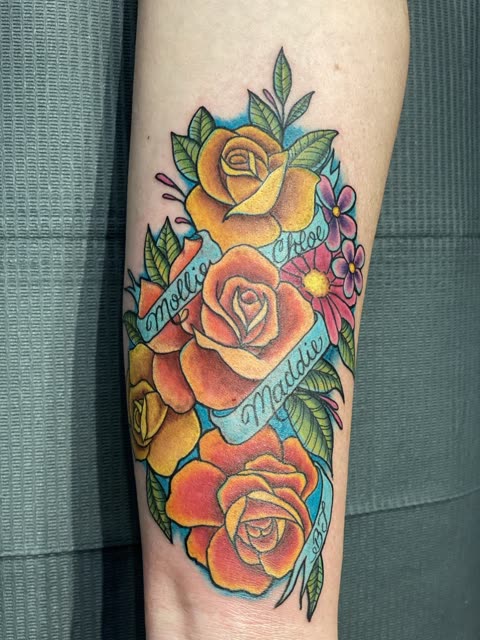 Yellow and orange roses tattoo wrapped in name banners, full color, down a forearm