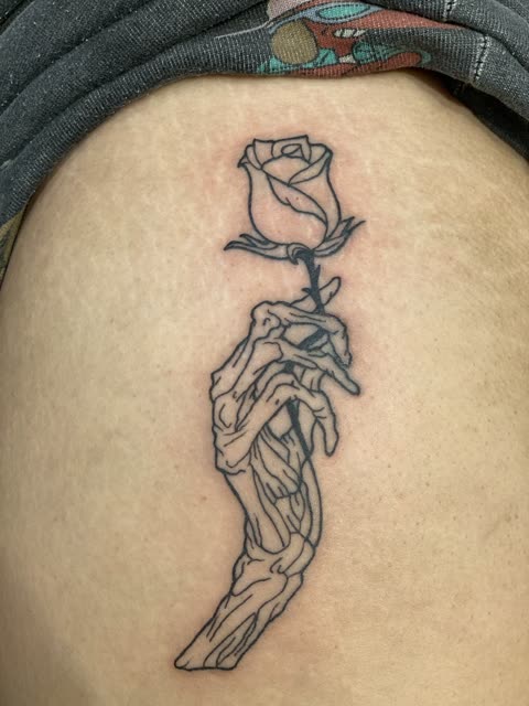 Skeleton hand holding a rose tattoo, clean linework, on the torso