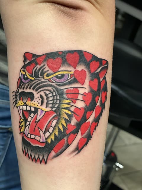 Traditional tiger head tattoo patterned with red hearts, full color, on a forearm