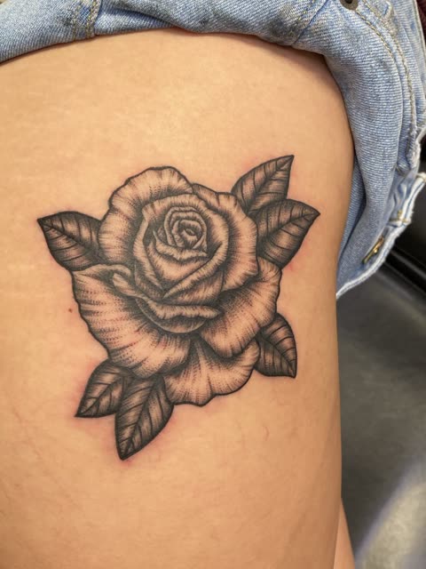 Full bloom rose tattoo in black stipple shading on a thigh