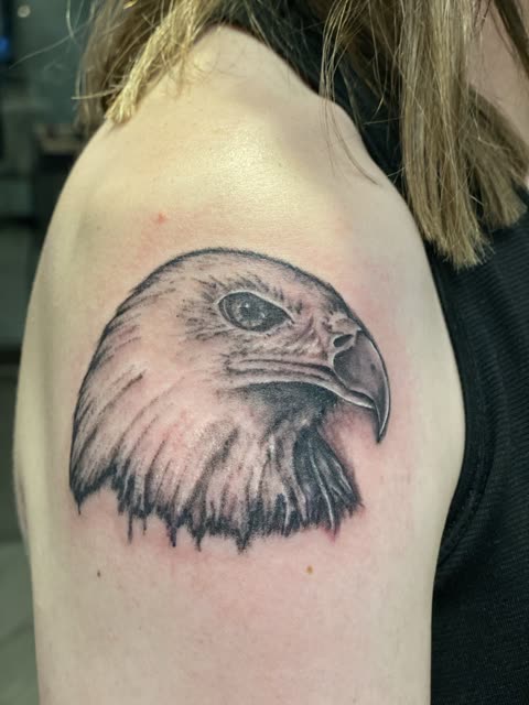 Eagle head tattoo in soft black shading on a shoulder