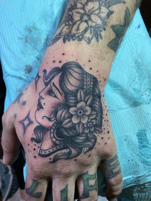 Traditional lady head tattoo with flowers in her hair, black shading, on the back of a hand