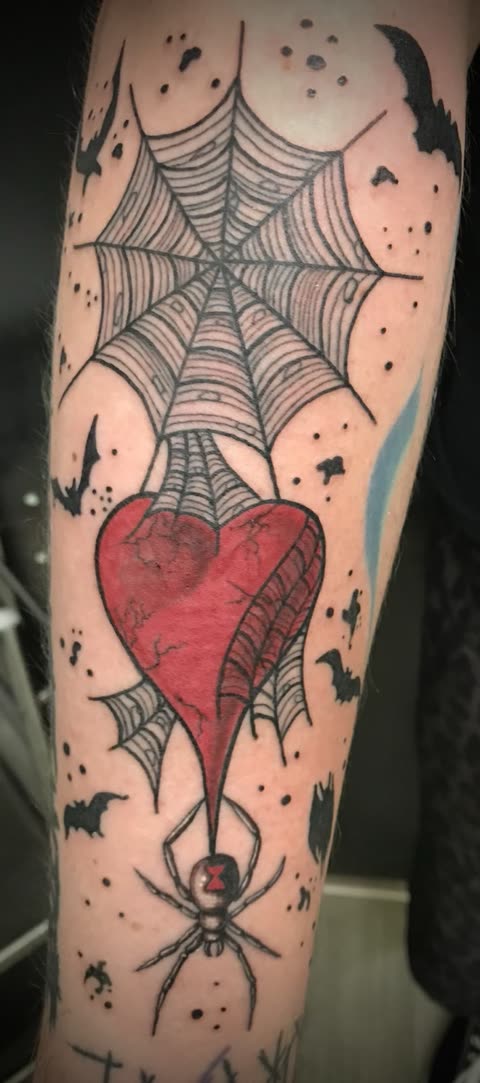 Spiderweb tattoo holding a red heart with a black widow spider and bats, on a forearm